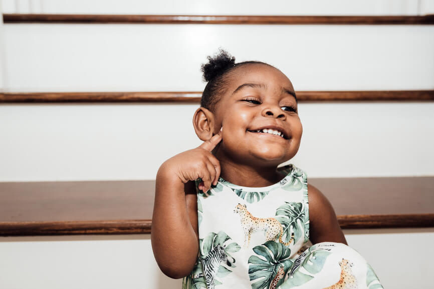 Young black girl sets on a staircase while smiling and pointing to her face