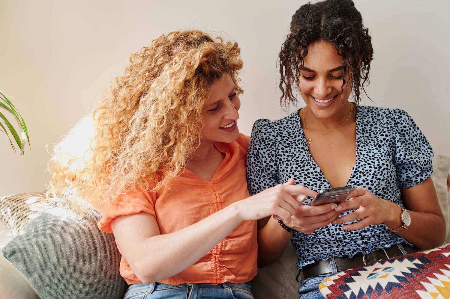Two smiling women point and look at a smartphone together