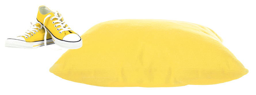 A yellow pillow lying on the ground with yellow sneakers