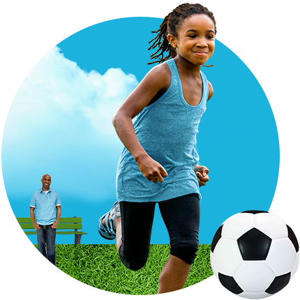 A boy plays with a soccer ball while his smiling father watches from a distance.