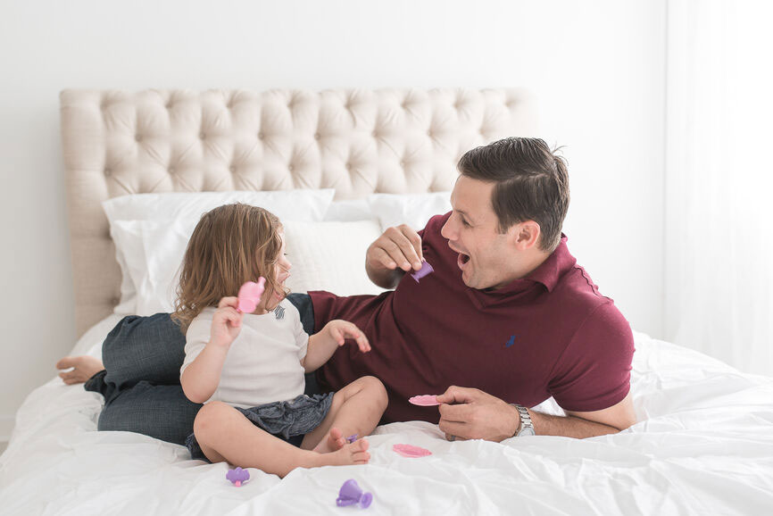 Dad and toddler have a pretend tea party on a bed