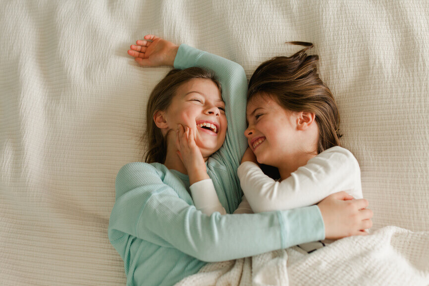 Twin sisters are playing and laughing on a bed